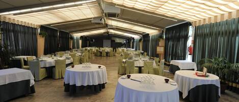 Un salón de banquetes con mesas redondas dispuestas para comer, cubiertas por un dosel a rayas y rodeadas de sillas verdes.