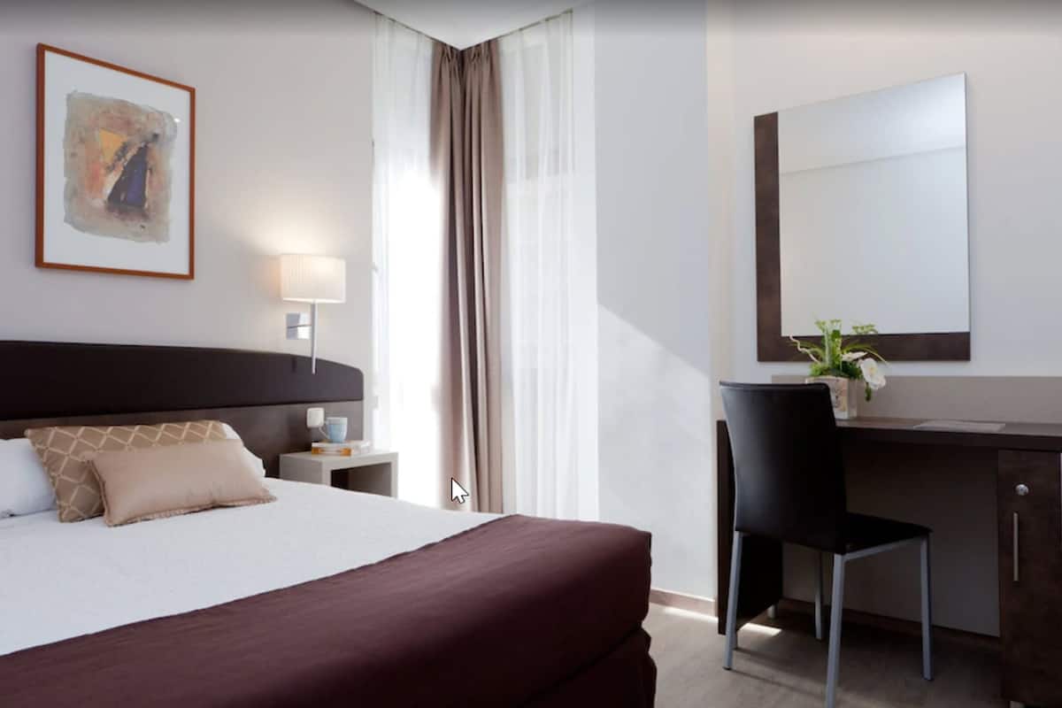 A hotel room with a large bed, a desk, a chair, a lamp, and a painting on the wall.