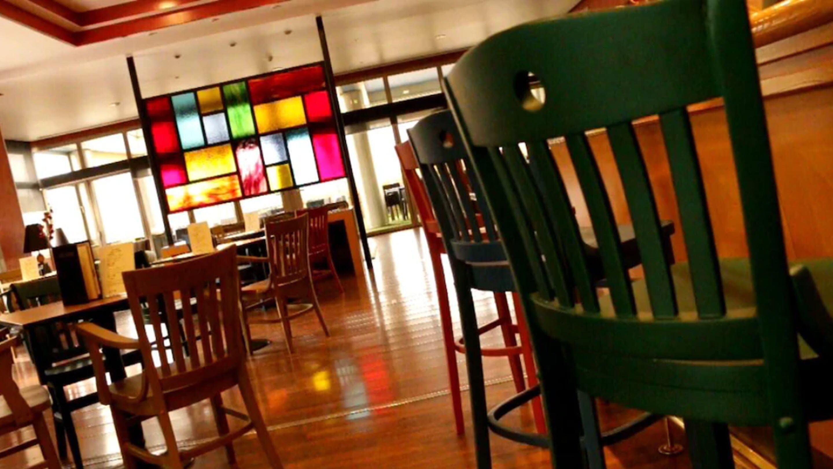 A restaurant interior with wooden tables and chairs, a colorful stained glass window, and a wooden ceiling.