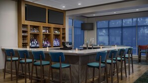 A bar area with a long counter, multiple stools, and a television mounted on the wall. - Hilton Garden Inn Orlando at SeaWorld (Orlando)