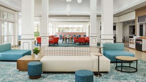 A spacious lobby with a central seating area, multiple tables, and a food kiosk. - Hilton Garden Inn Orlando at SeaWorld (Orlando)
