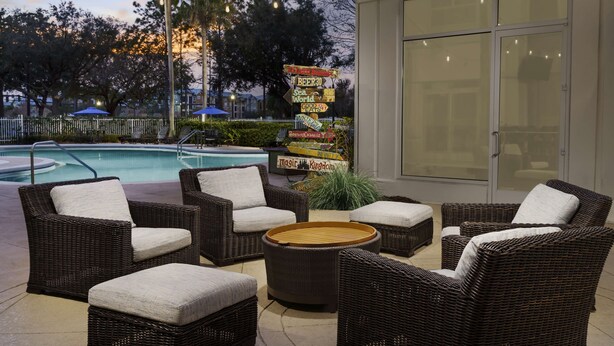 An outdoor seating area with wicker furniture, a pool, and a signpost with various directions. - Hilton Garden Inn Orlando at SeaWorld (Orlando)