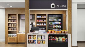 A store named 'The Shop' with shelves of snacks, a refrigerated section, and a coffee machine. - Hilton Garden Inn Orlando at SeaWorld (Orlando)
