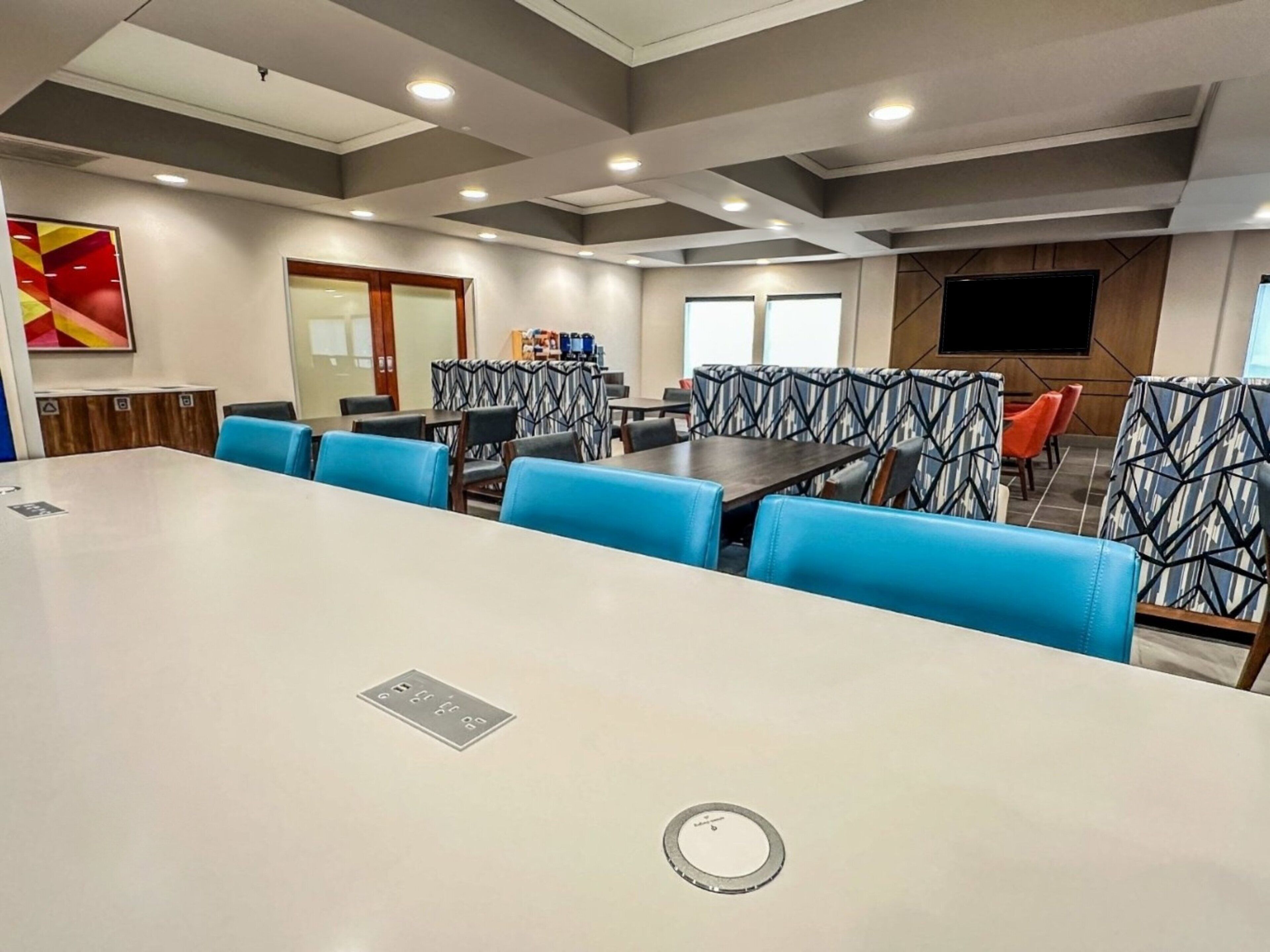 Una sala de conferencias con una gran mesa, sillas azules y una pantalla de televisión.