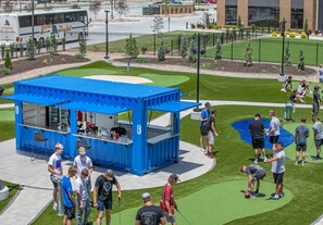 A blue food truck with a counter and seating area, surrounded by a grassy area with people around.