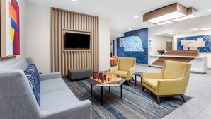 Eine moderne Lobby mit einer Couch, Sesseln, einem Schachtisch und einer Rezeption.