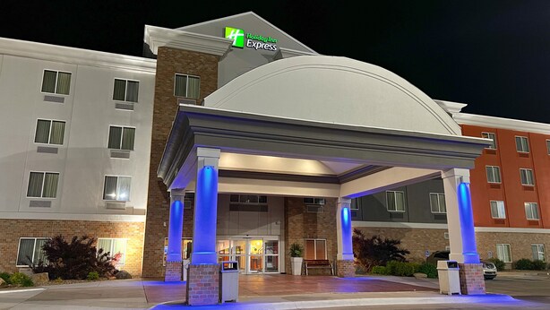 Ein Holiday Inn Express Hotel mit einem modernen Eingang, der durch blaue Beleuchtung und einen überdachten Zugang gekennzeichnet ist.