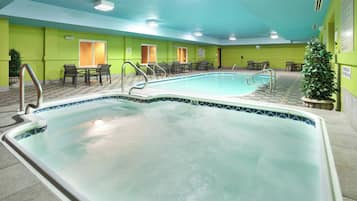 A swimming pool with a tiled edge, surrounded by chairs and tables, and a green wall with doors.