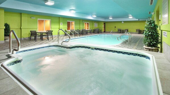 A swimming pool with a tiled edge, surrounded by chairs and tables, and a green wall with doors.