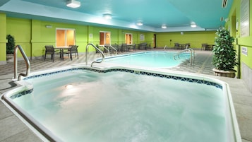 Una piscina con borde de azulejos, rodeada de sillas y mesas, y una pared verde con puertas.