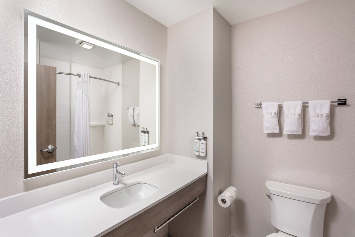 A modern bathroom with a large mirror, a white sink, a toilet, and a towel rack with towels.