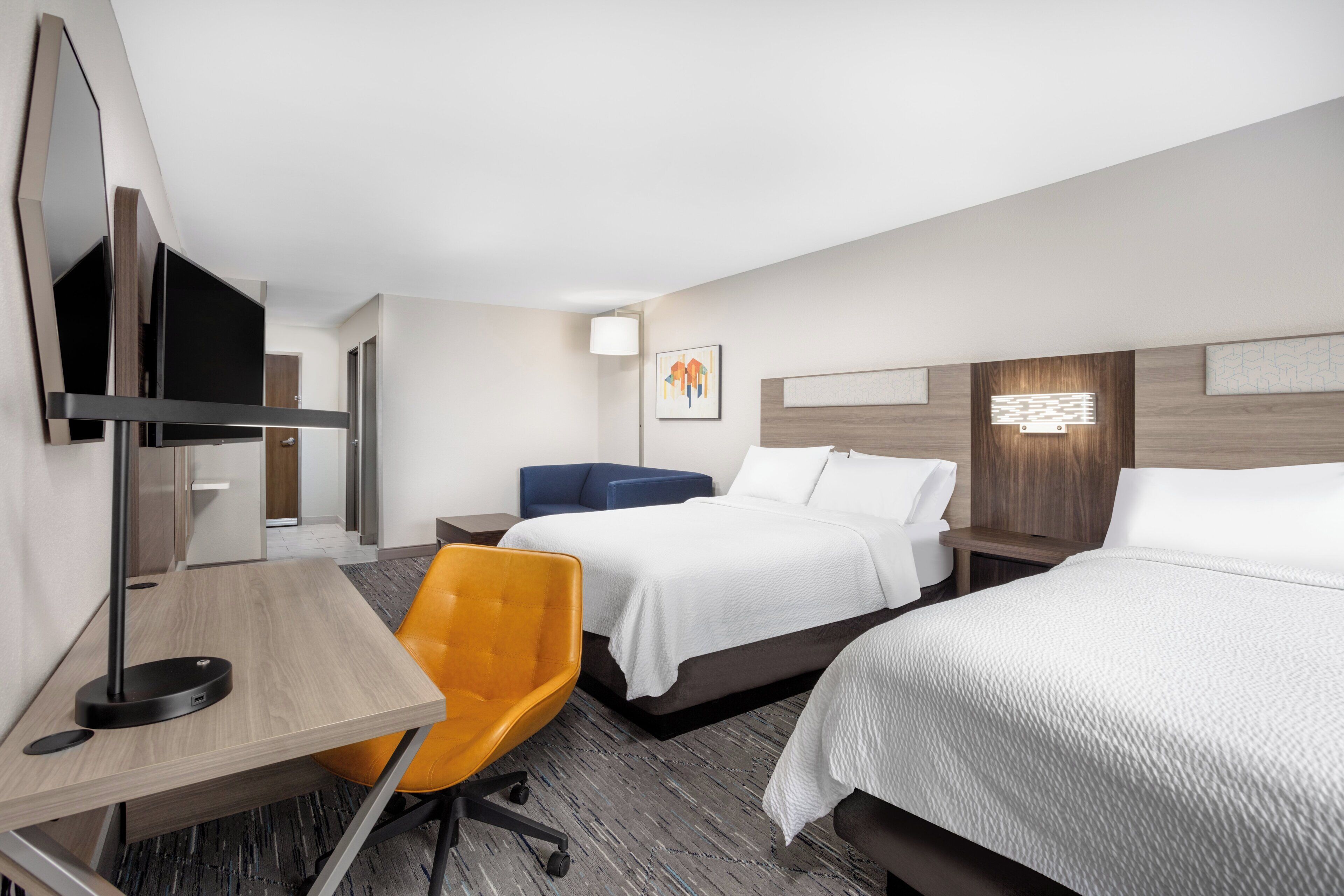 Habitación de hotel con cama, escritorio, silla, televisor y una obra de arte colgada en la pared.