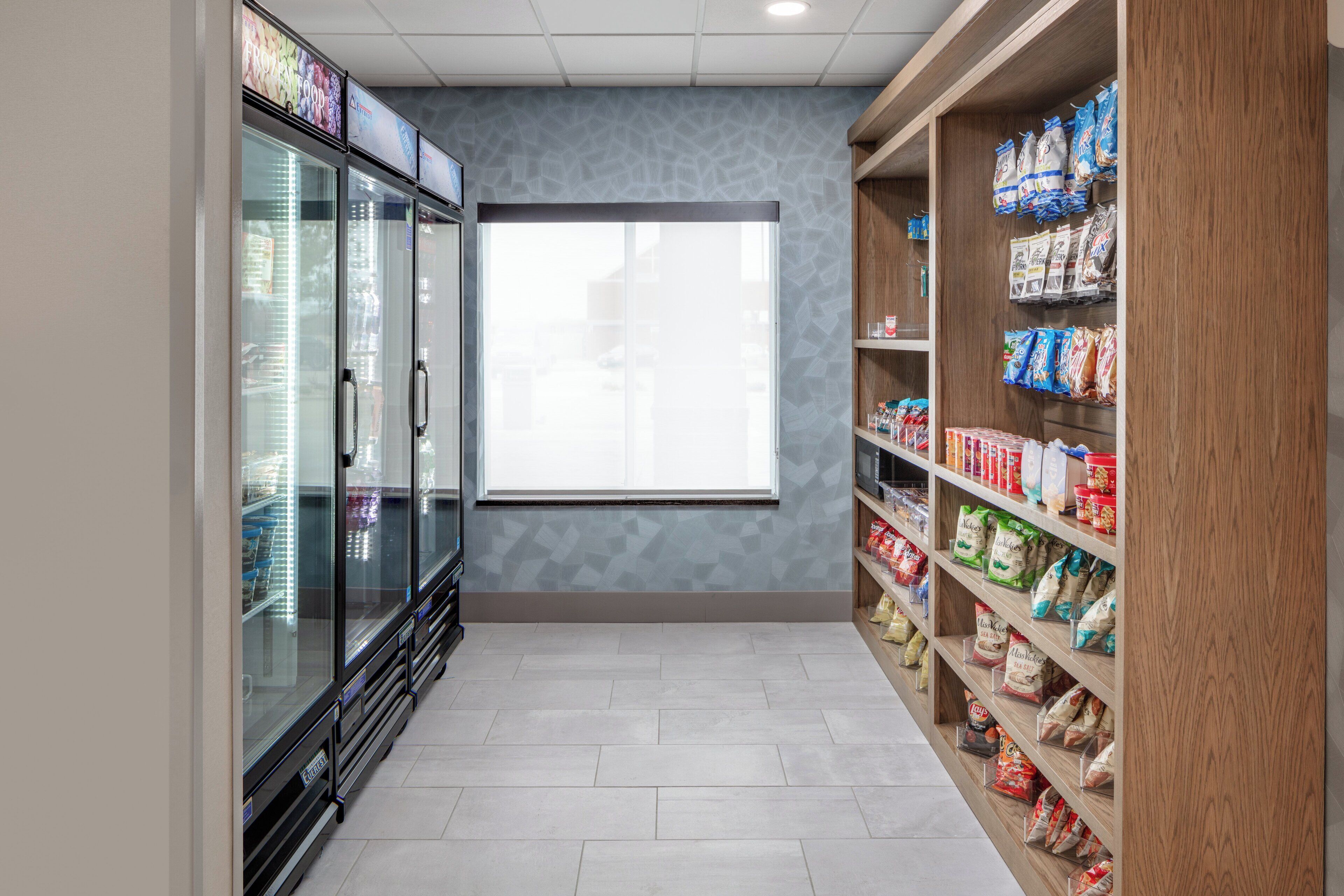 A corridor with a refrigerated display case on the left and shelves stocked with bags on the right.