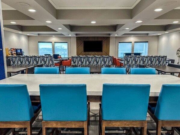 A conference room with a long table and blue chairs, a patterned wall, and a large TV screen. - Holiday Inn Express Kearney by IHG (Kearney)