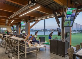 Zona de simulación de golf con varias pantallas, un putting green y vistas al río.