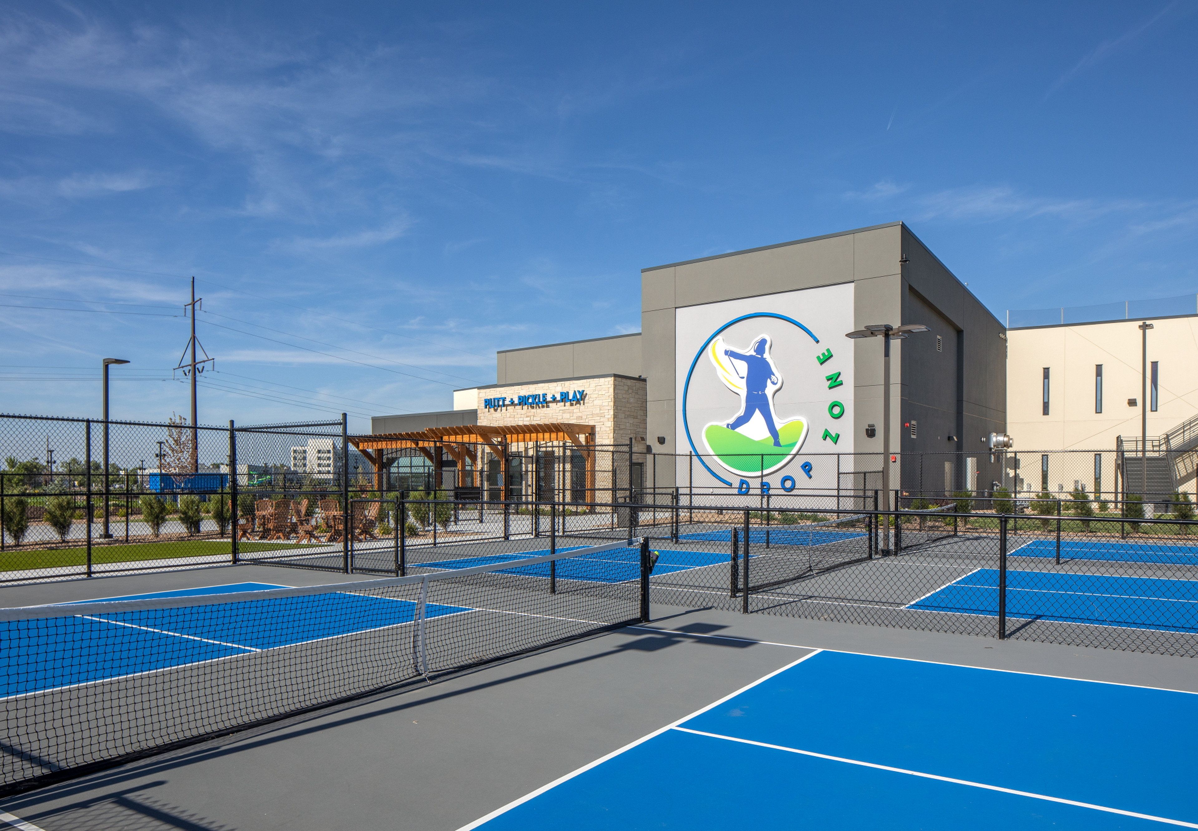 A sports facility with multiple tennis courts, a covered seating area, and a building with a large logo.
