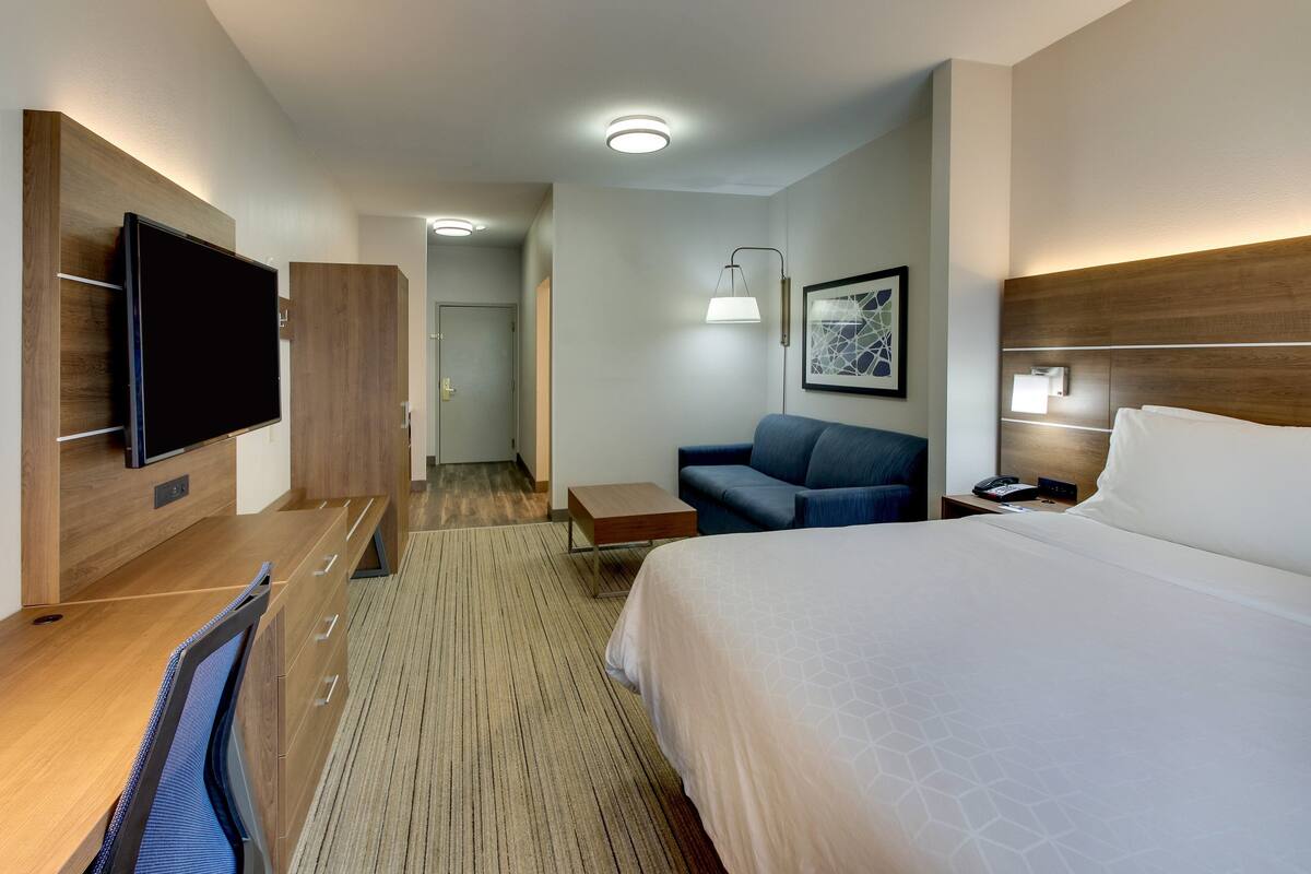 Ett hotellrum med en säng, ett skrivbord med en platt-TV, en soffa, ett litet bord och en vägglampa.
