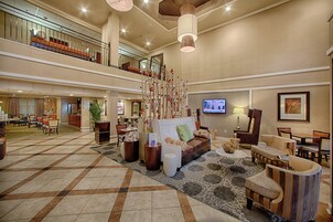 Un hall d’entrée spacieux avec un plafond haut, un espace de détente central avec un canapé et des fauteuils, un escalier et un écran de télévision fixé au mur.