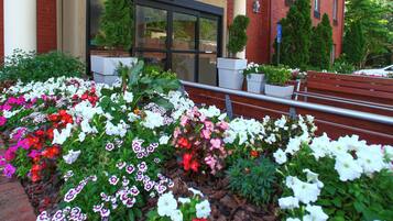 A building entrance with a brick facade, large windows, and a flower bed with various flowers.