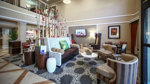 A spacious lobby with a high ceiling, a decorative tree sculpture, a comfortable seating area with sofas and armchairs, a television mounted on the wall, and a reception desk. - Holiday Inn Express Atlanta - Emory University Area by IHG (Decatur)