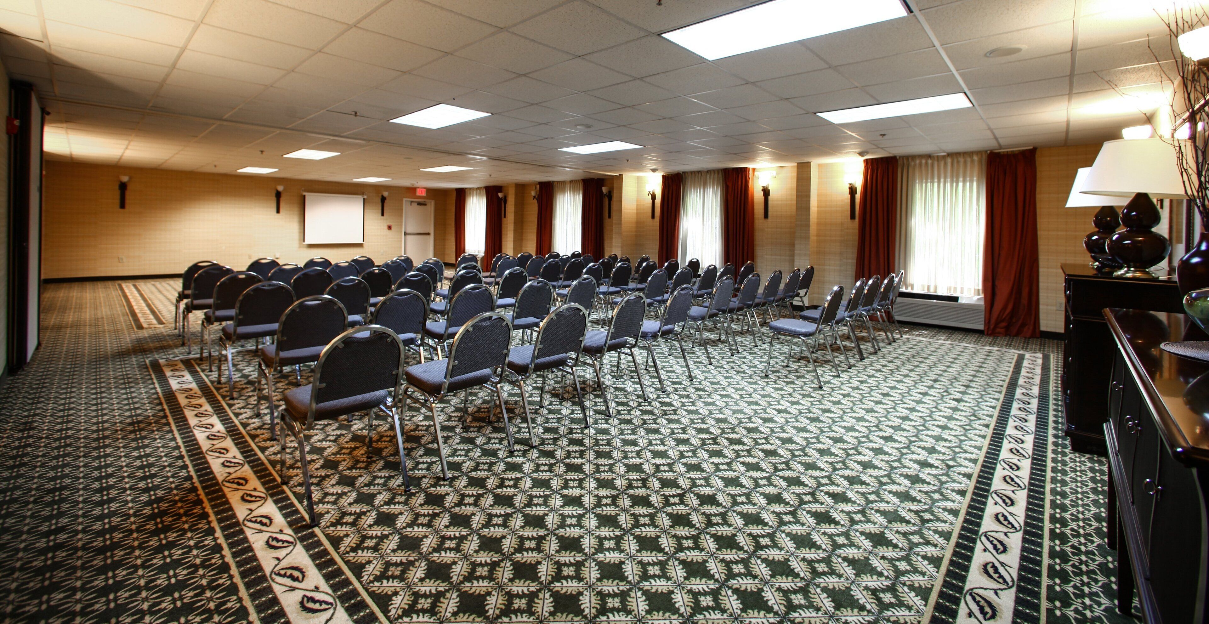 A conference room with rows of chairs, a projector screen, and a patterned carpet.