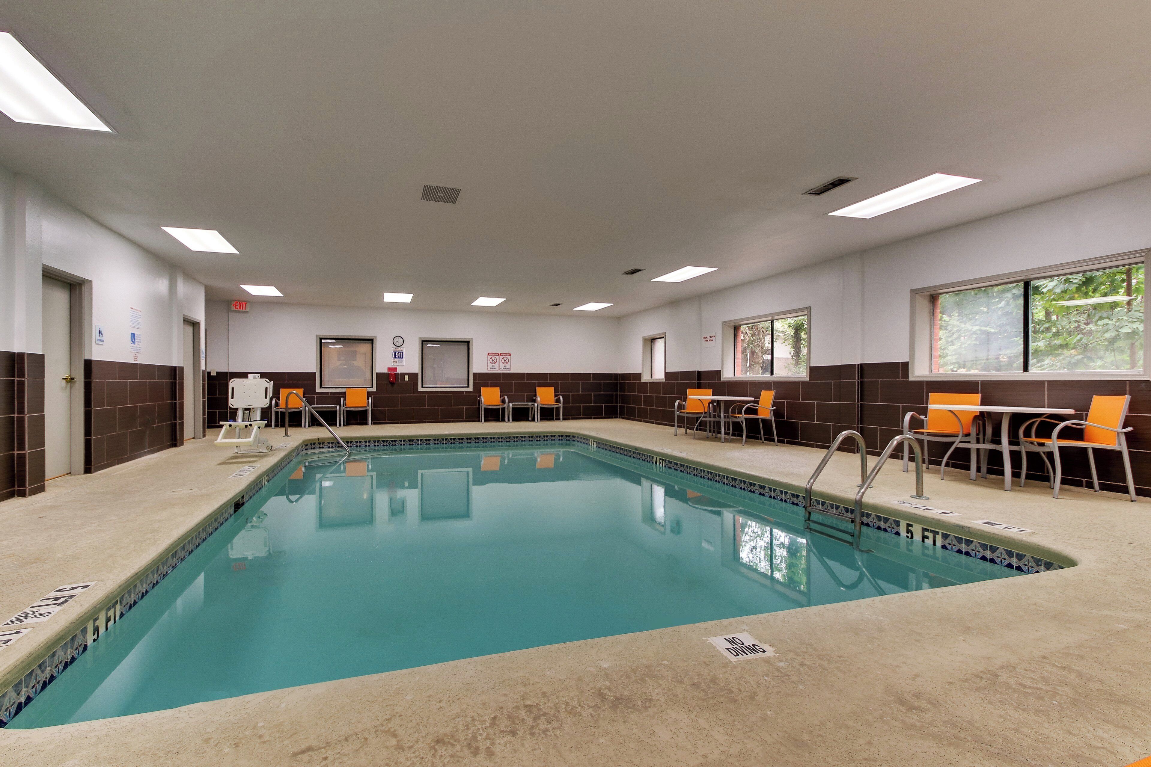 Una piscina con borde de azulejos, rodeada de sillas y mesas naranjas, y un letrero que indica una profundidad de 1,5 metros.