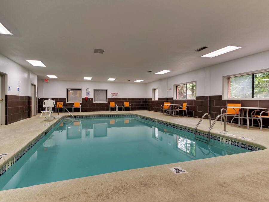 A swimming pool with a tiled edge, surrounded by orange chairs and tables, and a sign indicating a 5 ft depth.