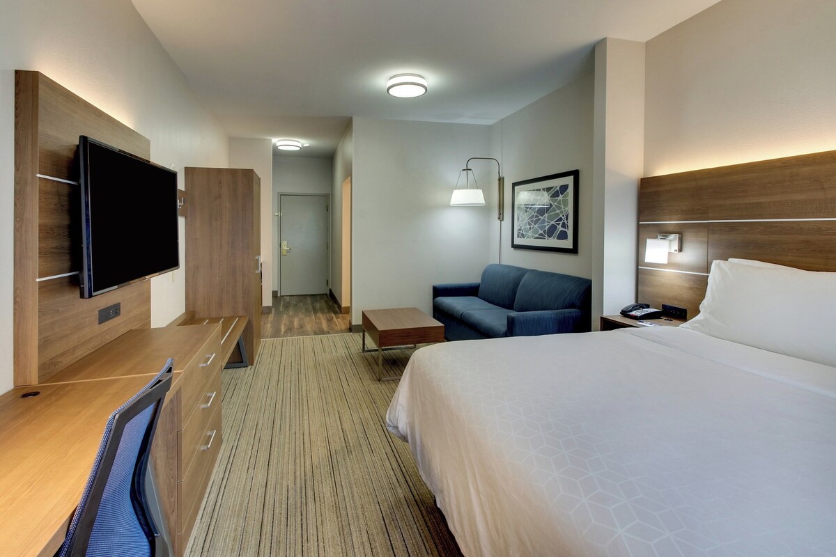 Une chambre d’hôtel comprenant un lit, un bureau avec un téléviseur à écran plat, un canapé, une petite table et une lampe fixée au mur.