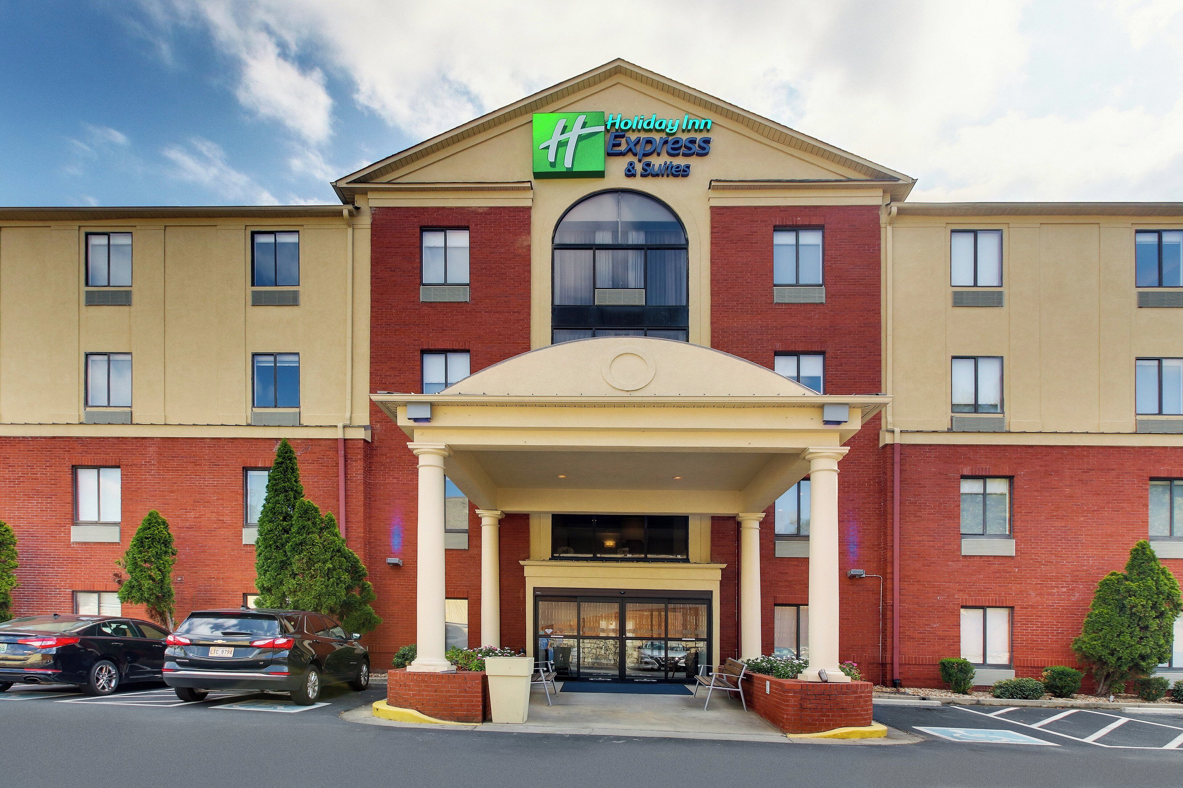 Un bâtiment de la chaîne Holiday Inn Express & Suites, avec une entrée principale, un parking et un ciel dégagé.