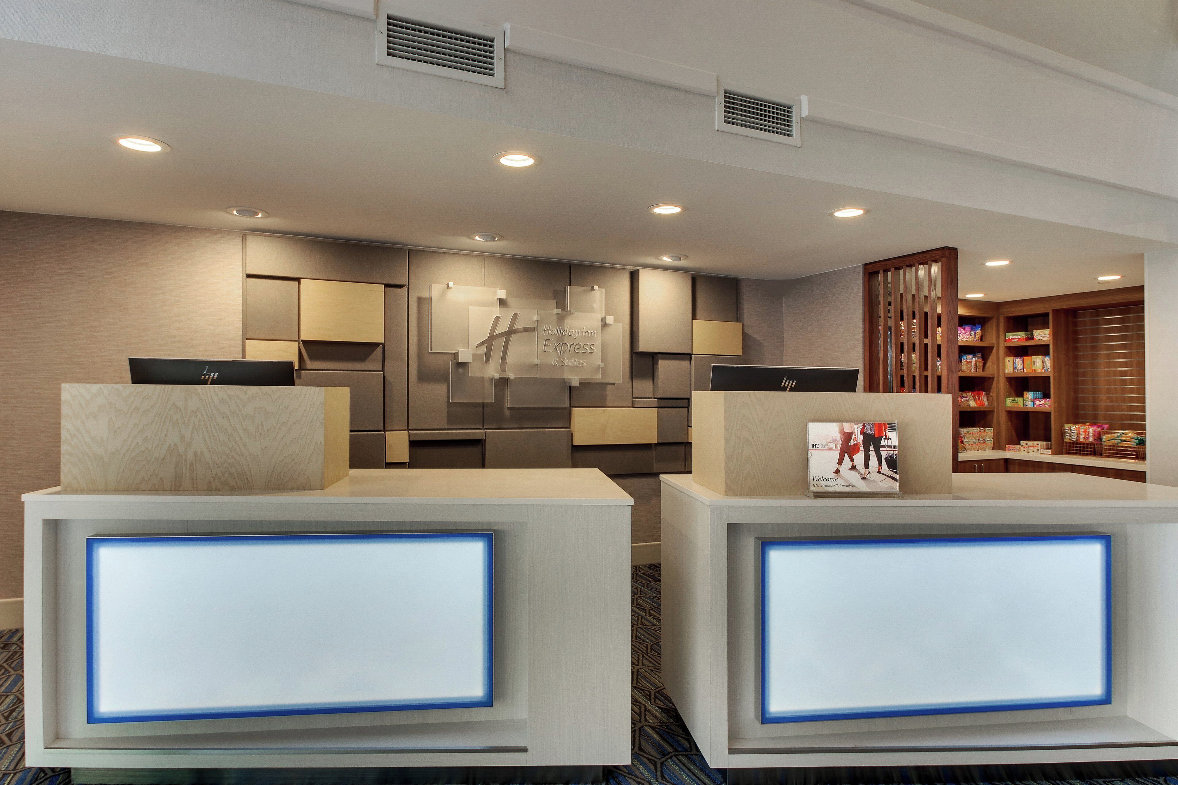 A hotel reception area with a modern design, featuring a reception desk, a wall-mounted sign, and a display of amenities.