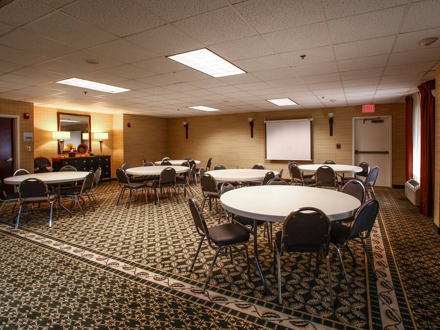 A conference room with multiple tables and chairs, a projector screen, and a carpeted floor.