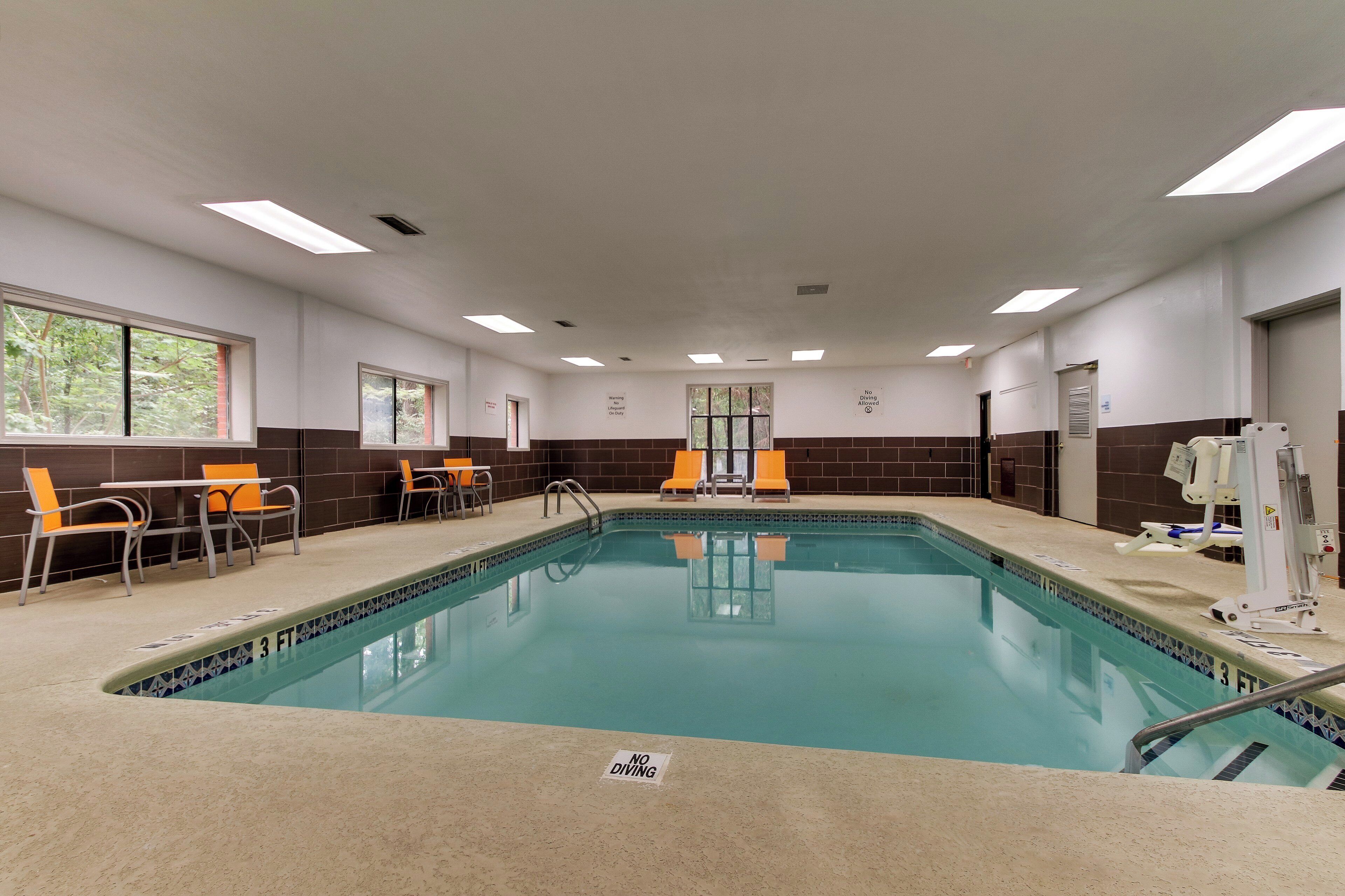 Ein Swimmingpool mit einer Tiefenmarkierung von 3 Fuß, umgeben von orangefarbenen Stühlen und Tischen, mit Blick auf Bäume durch die Fenster.