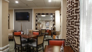A hotel dining area with a television, multiple tables and chairs, and a patterned wall. - Holiday Inn Express Atlanta - Emory University Area by IHG (Decatur)