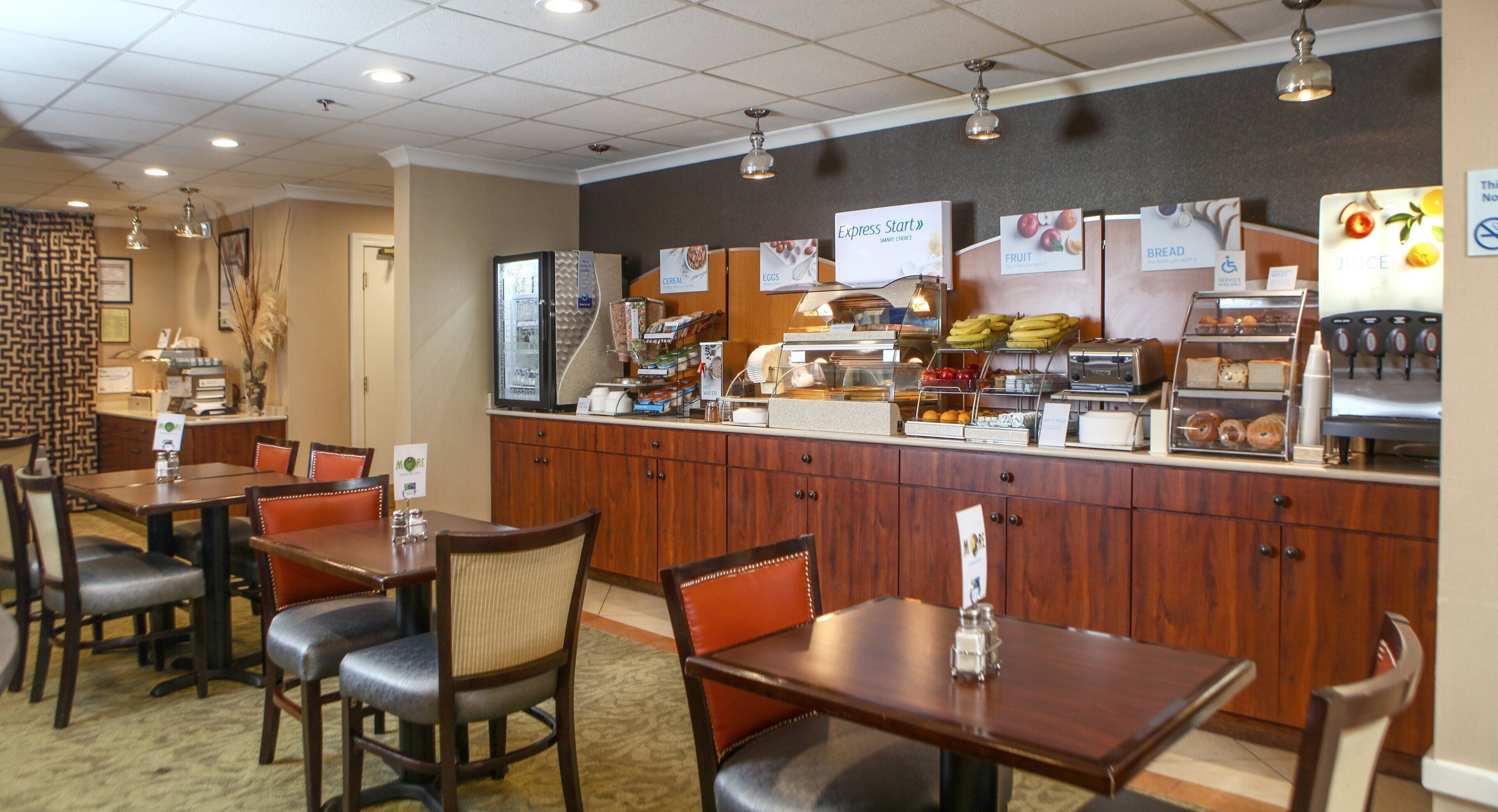 Zona de desayuno de hotel con una barra de buffet, disposición de asientos y diversas opciones de comida.