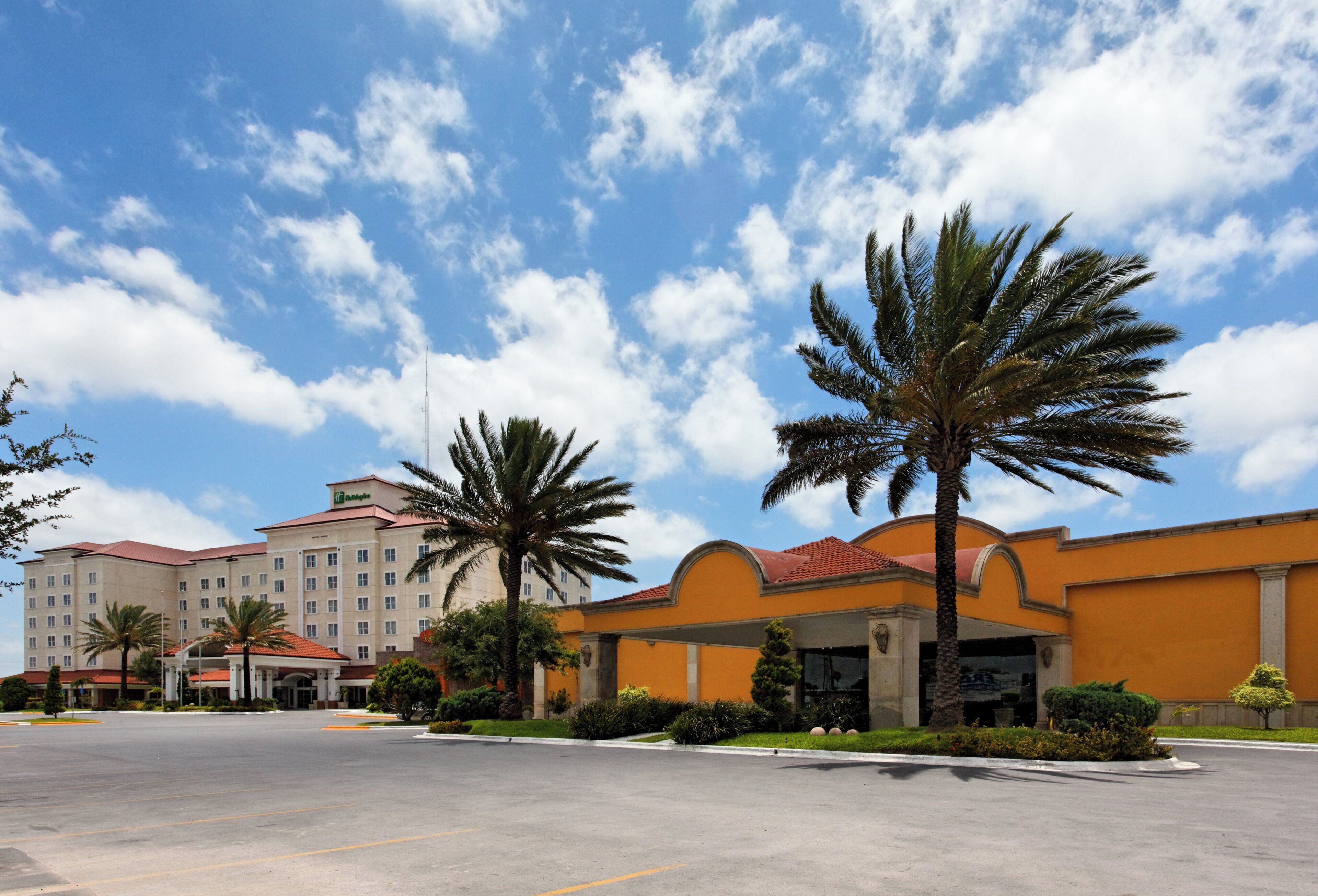 A hotel with a parking lot, palm trees, and a clear sky.