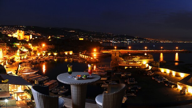 A waterfront hotel with a dining area, outdoor seating, and boats docked by the water. - Byblos Sur Mer (Byblos)