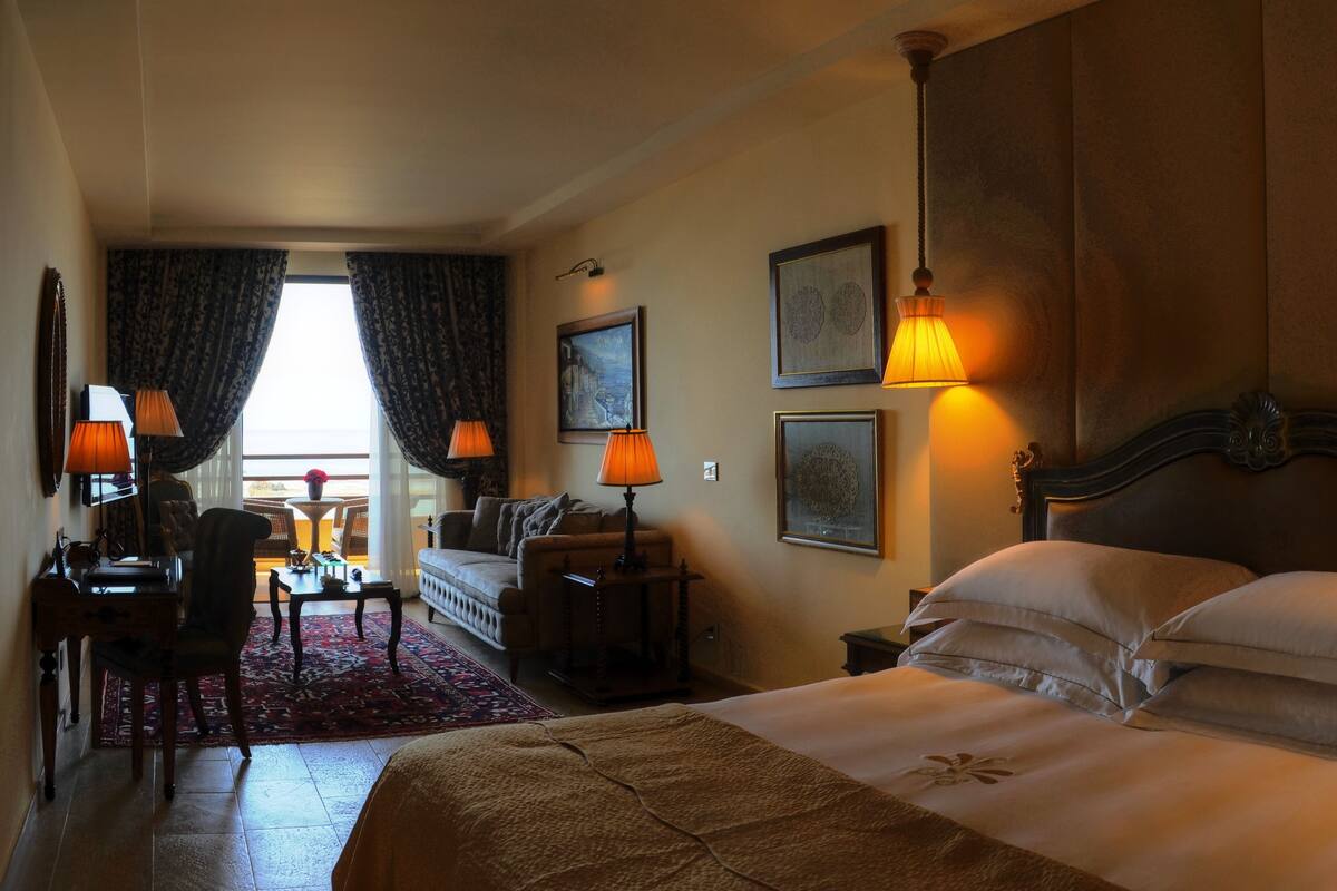 Habitación de hotel con cama, sofá, escritorio con lámpara y vistas al exterior.