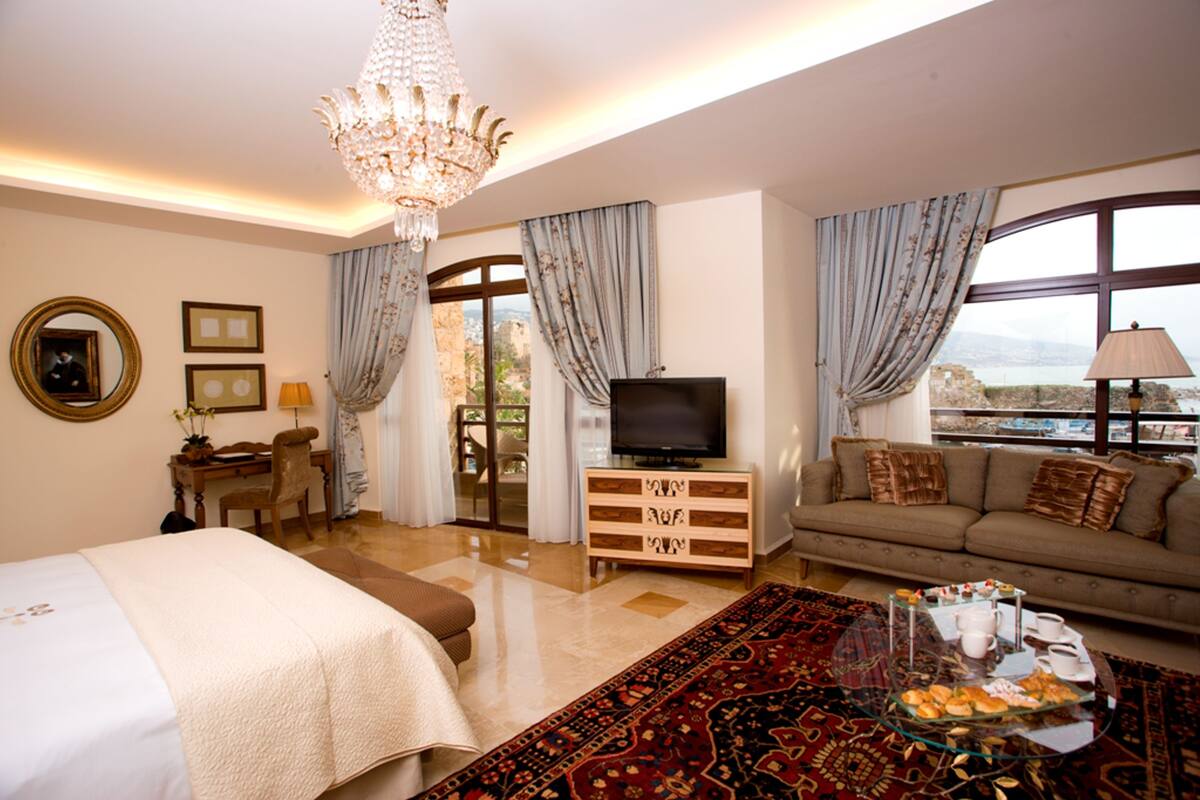 Habitación de hotel con cama, sofá, televisor, escritorio con silla, candelabro y vista al exterior.