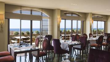 A restaurant with tables and chairs, large windows with a view of the sea, and a modern interior design.