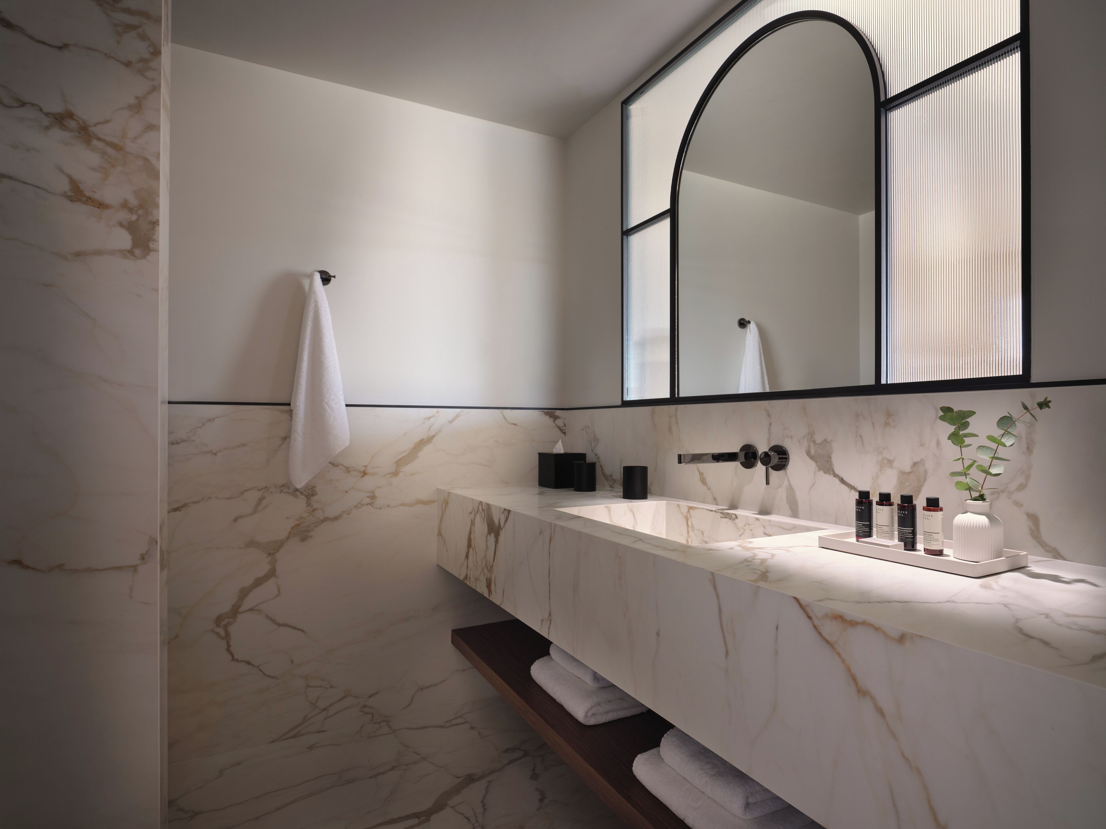 A modern bathroom with a marble sink, a large mirror, and a towel rack.