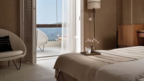A bedroom with a bed, a chair, a lamp, and a view of the sea through a sliding door.