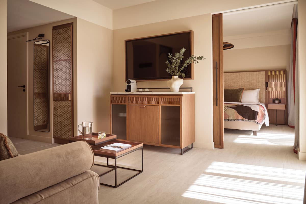 A modern hotel room with a sofa, a coffee table, a TV, a wooden cabinet, and a bed with a headboard.