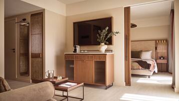 A modern hotel room with a wooden cabinet, a flat-screen TV, a sofa, and a bed with a headboard.