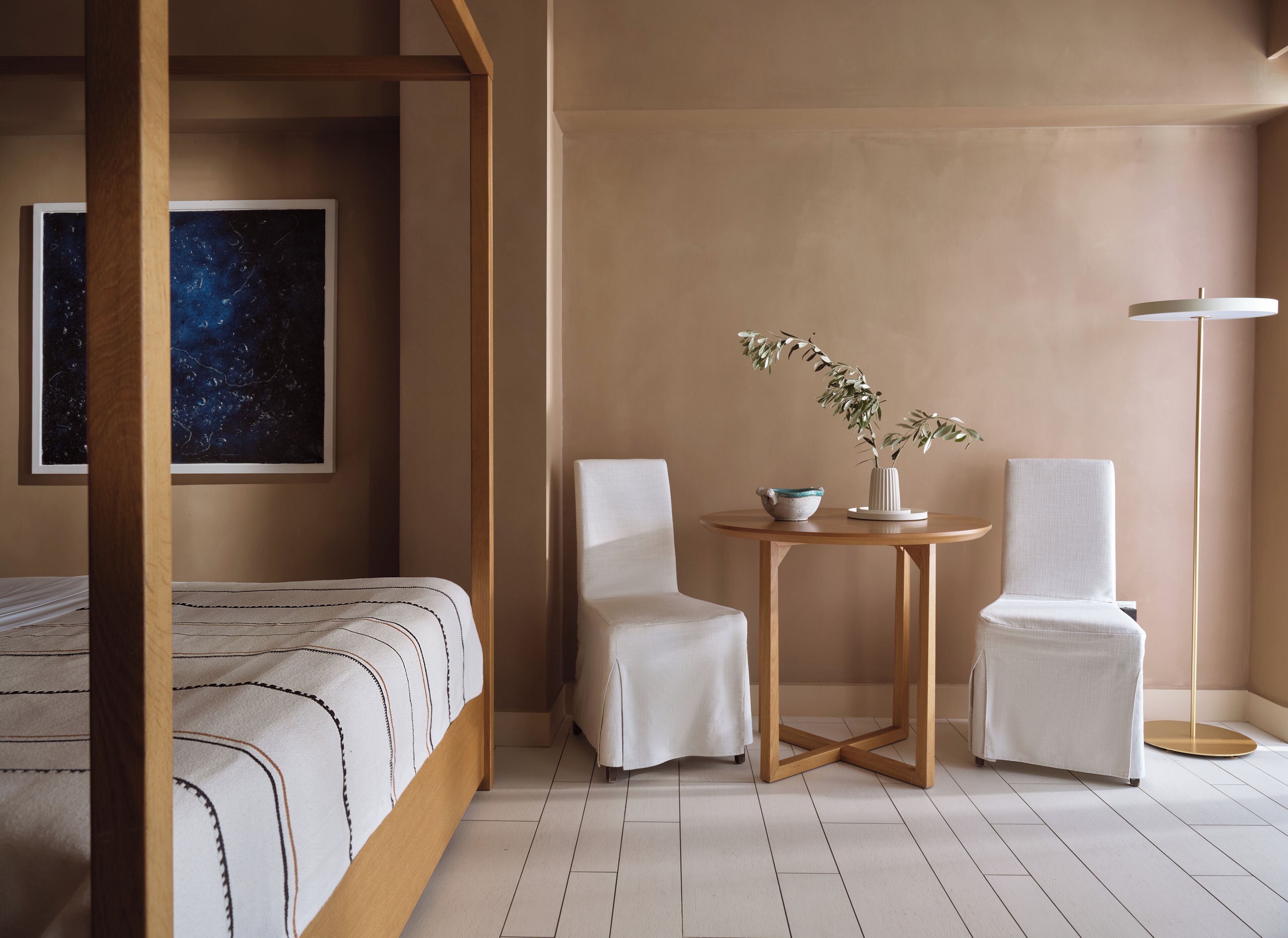 A bedroom with a four-poster bed, a round wooden table with chairs, a floor lamp, and a painting of a starry night on the wall.