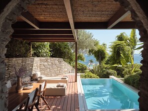 A poolside area with a stone wall, wooden deck, and a view of the sea. - Eagles Palace - Small Luxury Hotels of the World (Aristotelis)