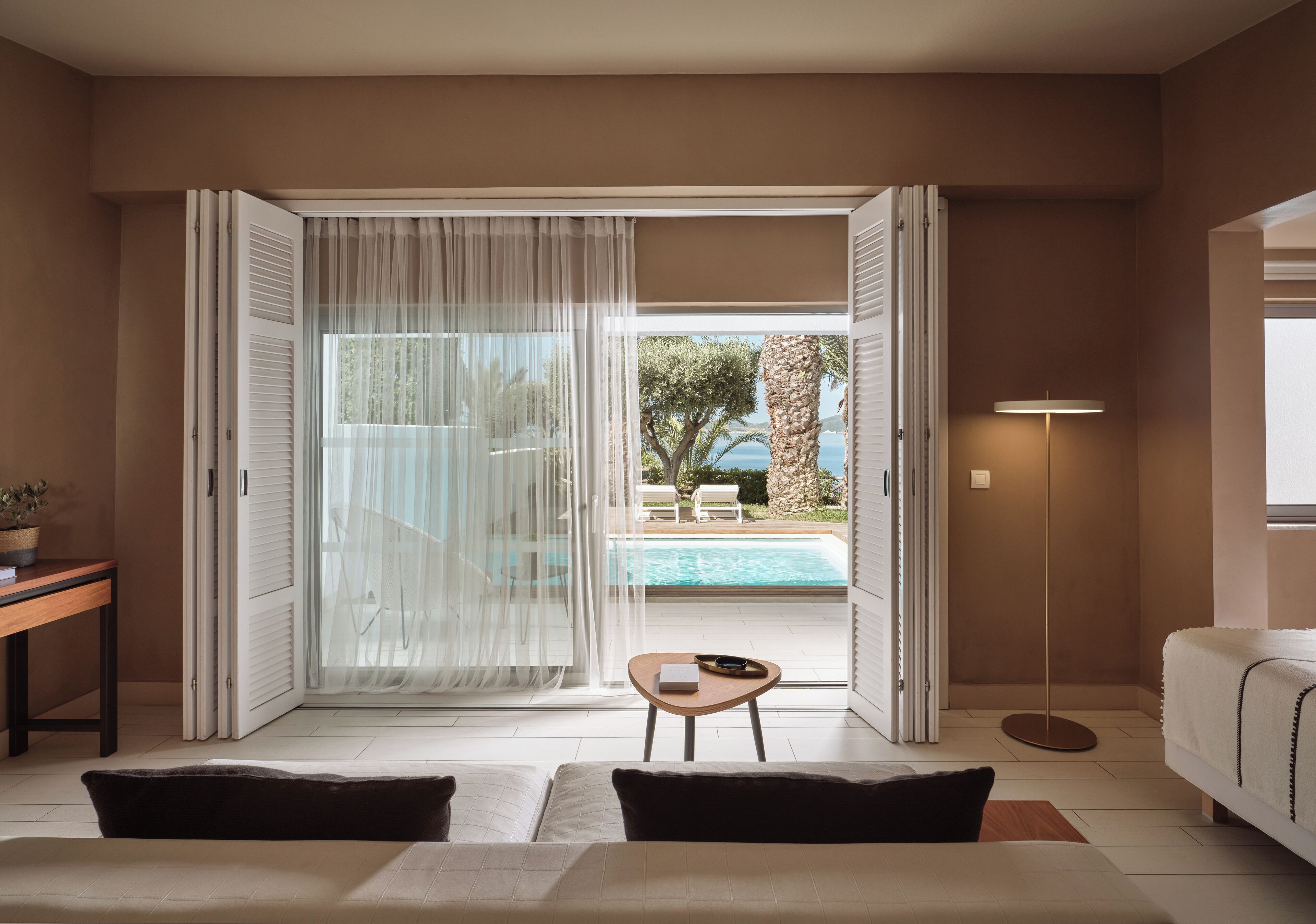 A bedroom with a view of a pool and outdoor seating.