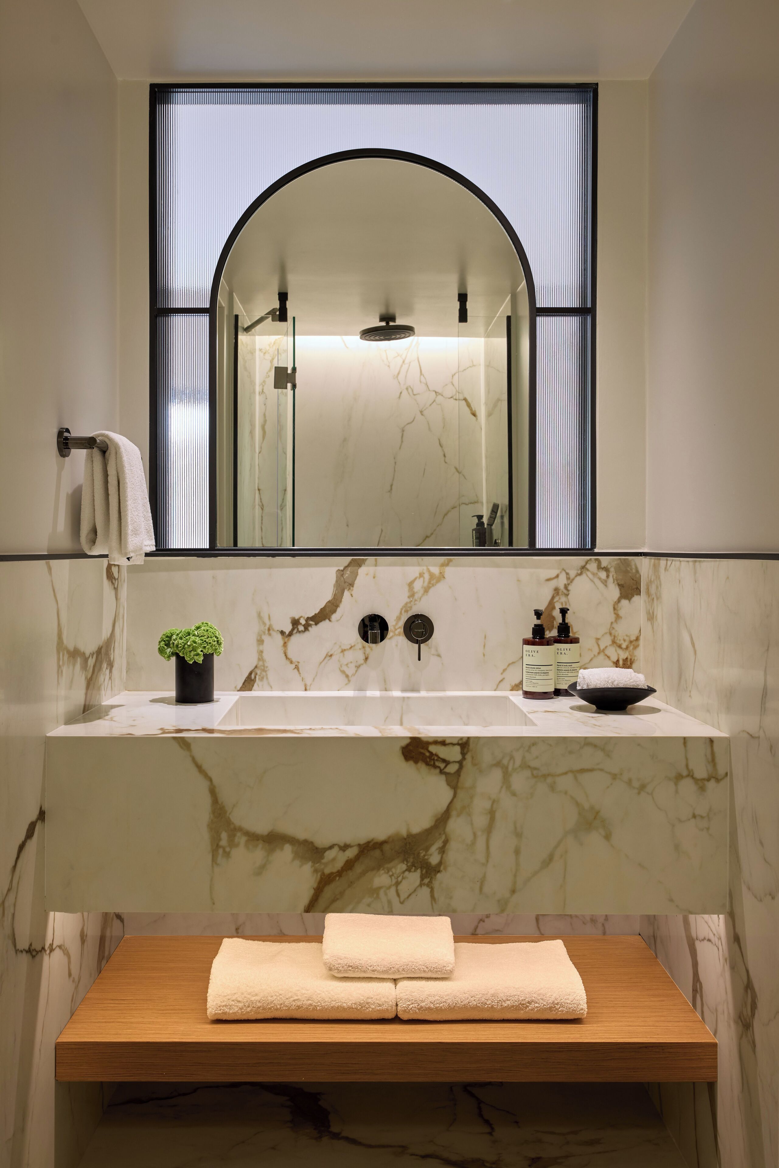 A bathroom with a marble sink, a wooden vanity, a mirror with an arched top, and a small potted plant.