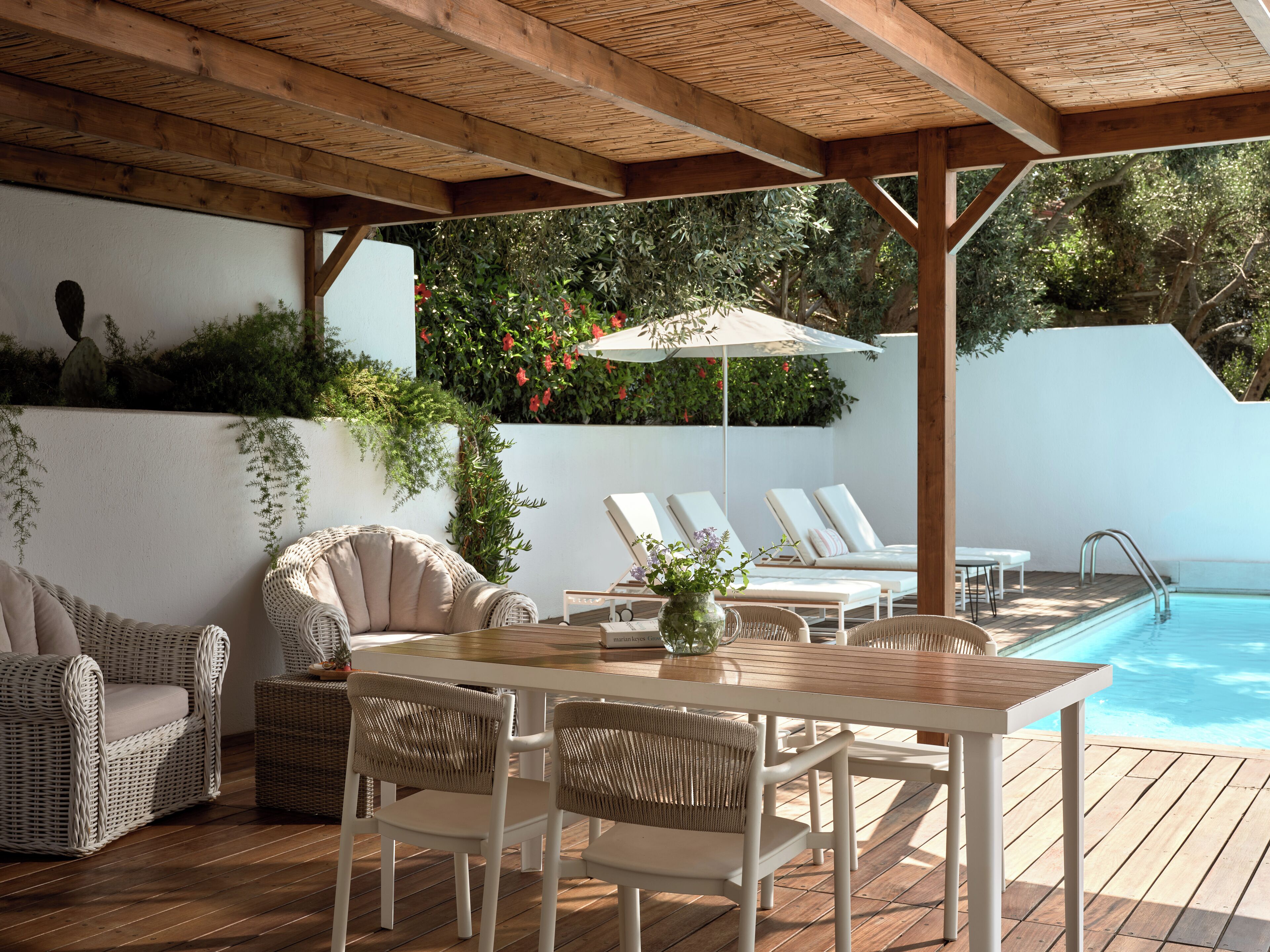 Un espacio exterior techado con piscina, muebles de mimbre y una mesa con un jarrón.