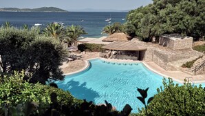 A pool area with a bar, lounge chairs, and a view of the sea.