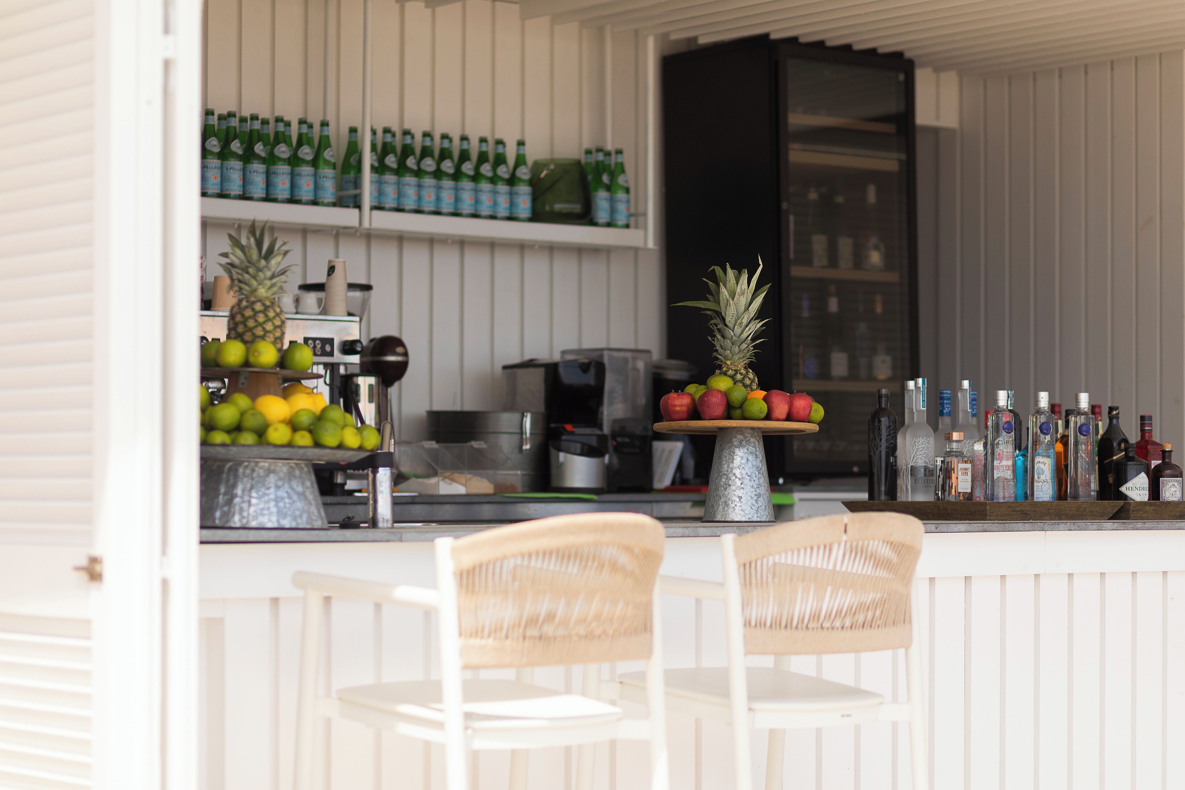 Cocina con armarios blancos, barra con botellas y una exhibición de fruta.